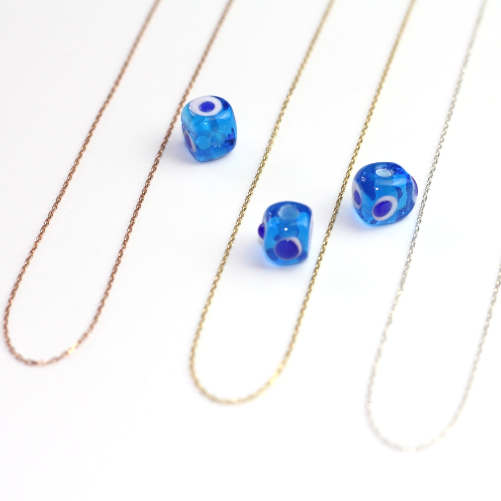 Yakın çekim, küp şeklinde el yapımı cam nazar boncuğu kolye ucu. Kolye ucu cam sanatı ürünüdür ve 0,5 köşe uzunluğundadır. Ürün, ortasından geçen 50 cm gümüş, altın veya rose rengi zincirle gösteriliyor.