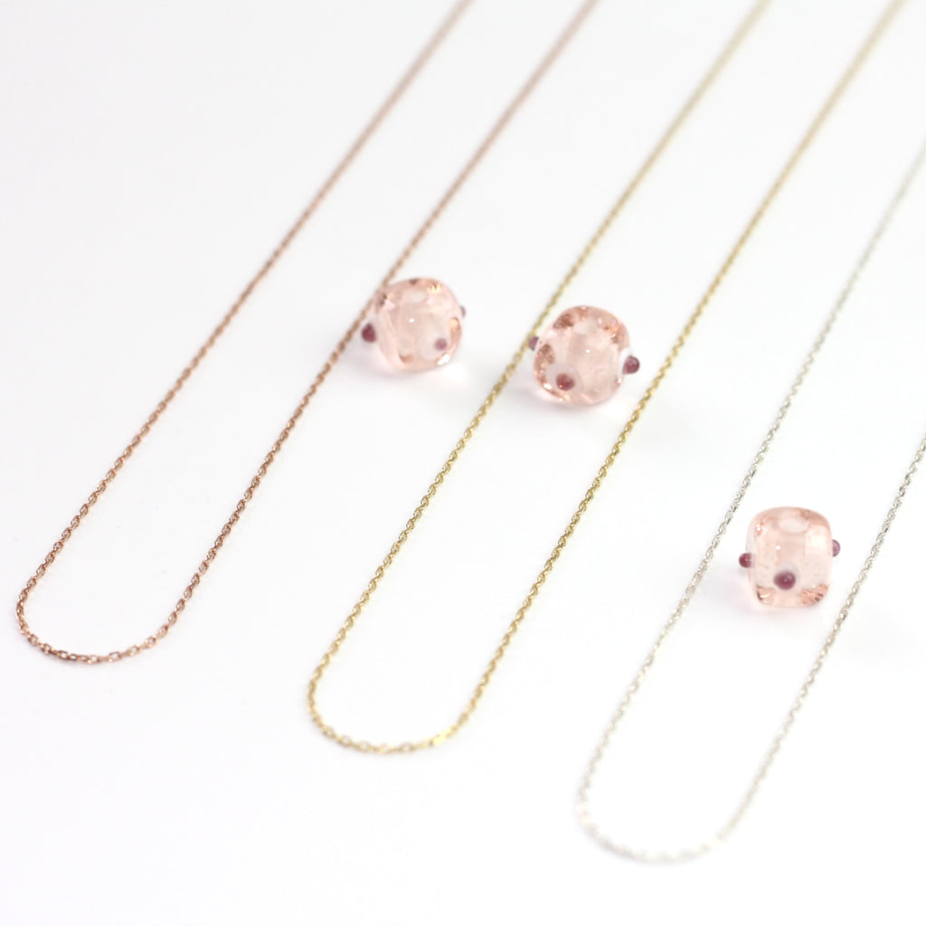 Yakın çekim, küp şeklinde el yapımı cam nazar boncuğu kolye ucu. Kolye ucu cam sanatı ürünüdür ve 0,5 köşe uzunluğundadır. Ürün, ortasından geçen 50 cm gümüş, altın veya rose rengi zincirle gösteriliyor.