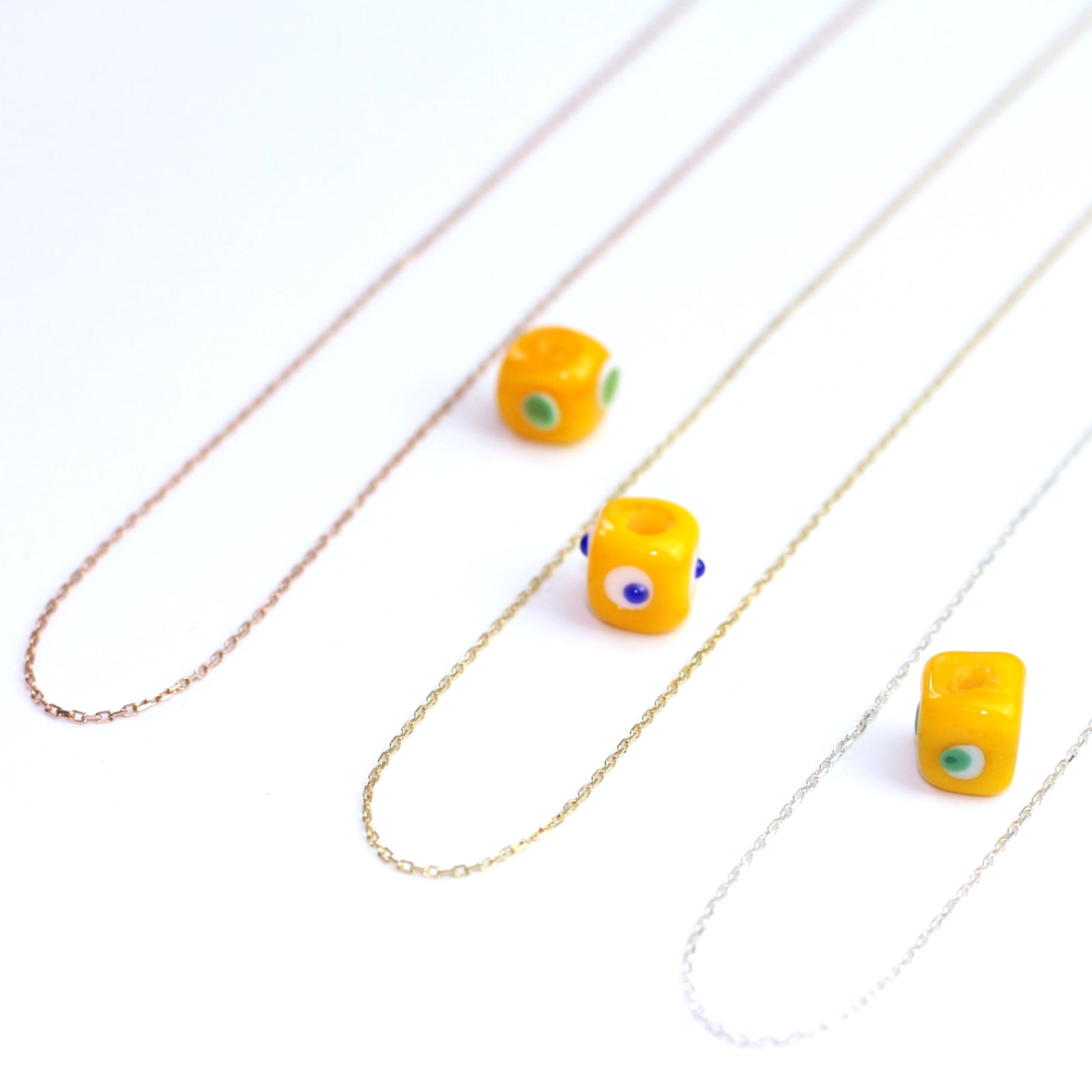 Yakın çekim, küp şeklinde el yapımı cam nazar boncuğu kolye ucu. Kolye ucu cam sanatı ürünüdür ve 0,5 köşe uzunluğundadır. Ürün, ortasından geçen 50 cm gümüş, altın veya rose rengi zincirle gösteriliyor.