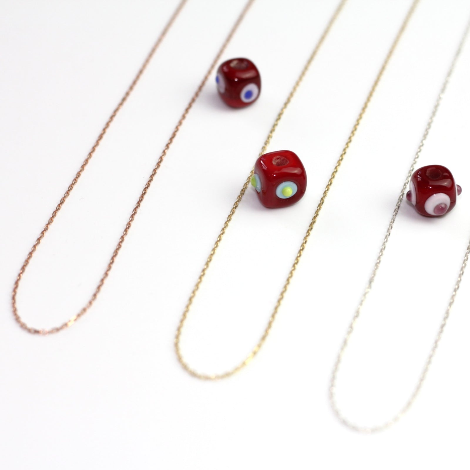 Yakın çekim, küp şeklinde el yapımı cam nazar boncuğu kolye ucu. Kolye ucu cam sanatı ürünüdür ve 0,5 köşe uzunluğundadır. Ürün, ortasından geçen 50 cm gümüş, altın veya rose rengi zincirle gösteriliyor.