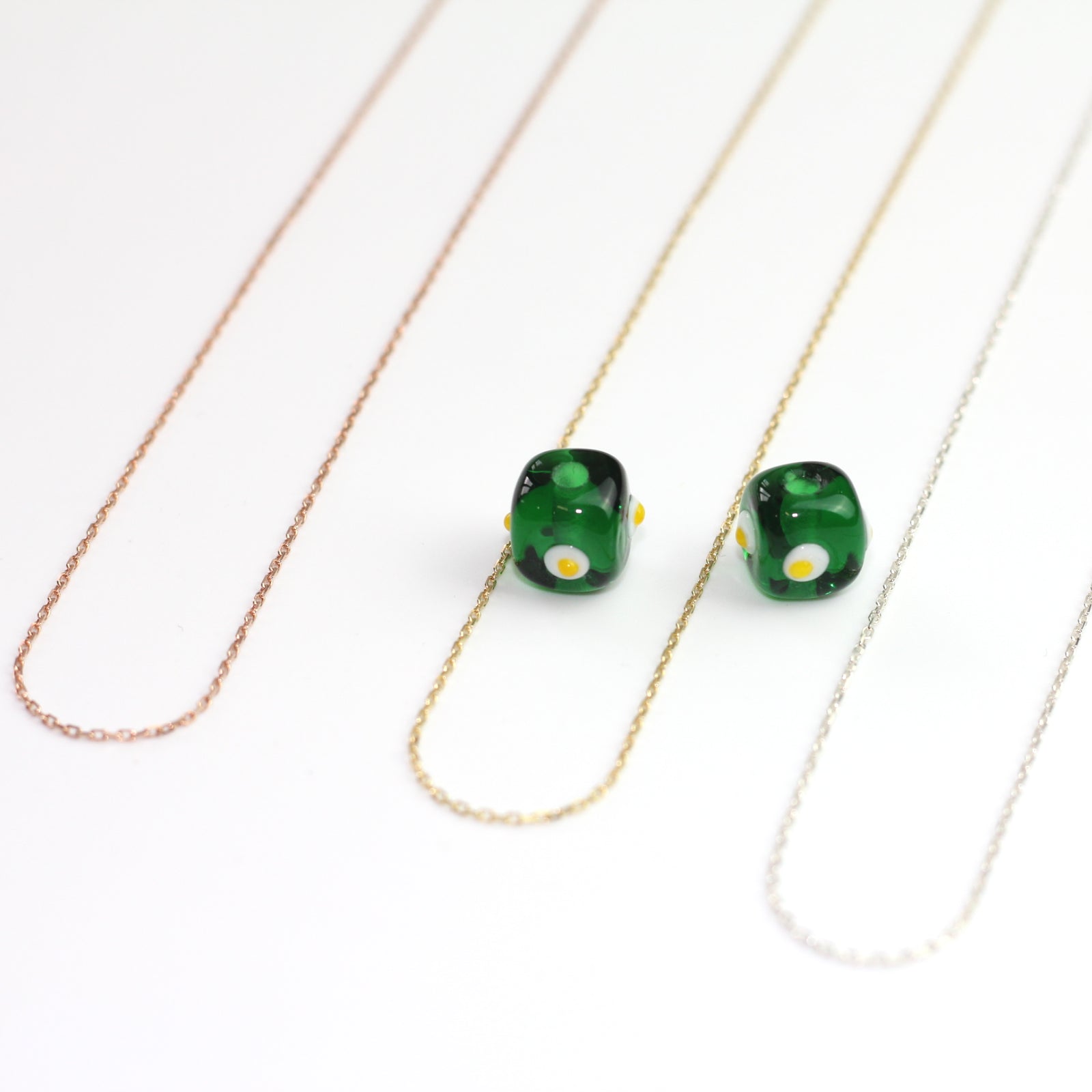 Yakın çekim, küp şeklinde el yapımı cam nazar boncuğu kolye ucu. Kolye ucu cam sanatı ürünüdür ve 0,5 köşe uzunluğundadır. Ürün, ortasından geçen 50 cm gümüş, altın veya rose rengi zincirle gösteriliyor.